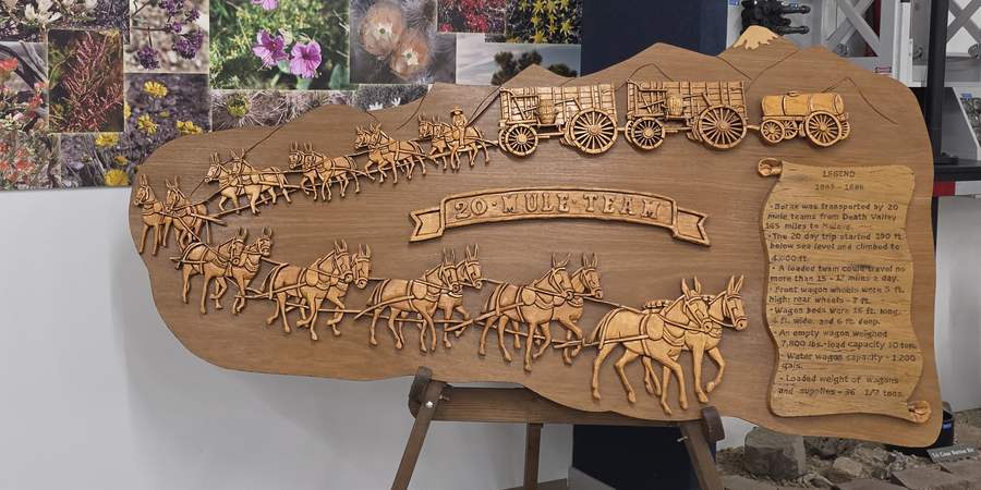 Carved wooden relief of a twenty-mule team hauling three borax wagons.