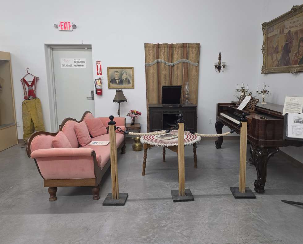 The museum parlor with a pink settee, a square grand piano and a framed portrait.